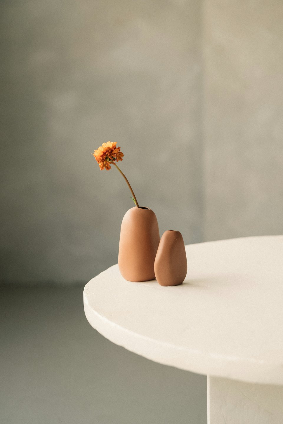 To terrakottavaser med en enkelt blomst på et teksturert bord.