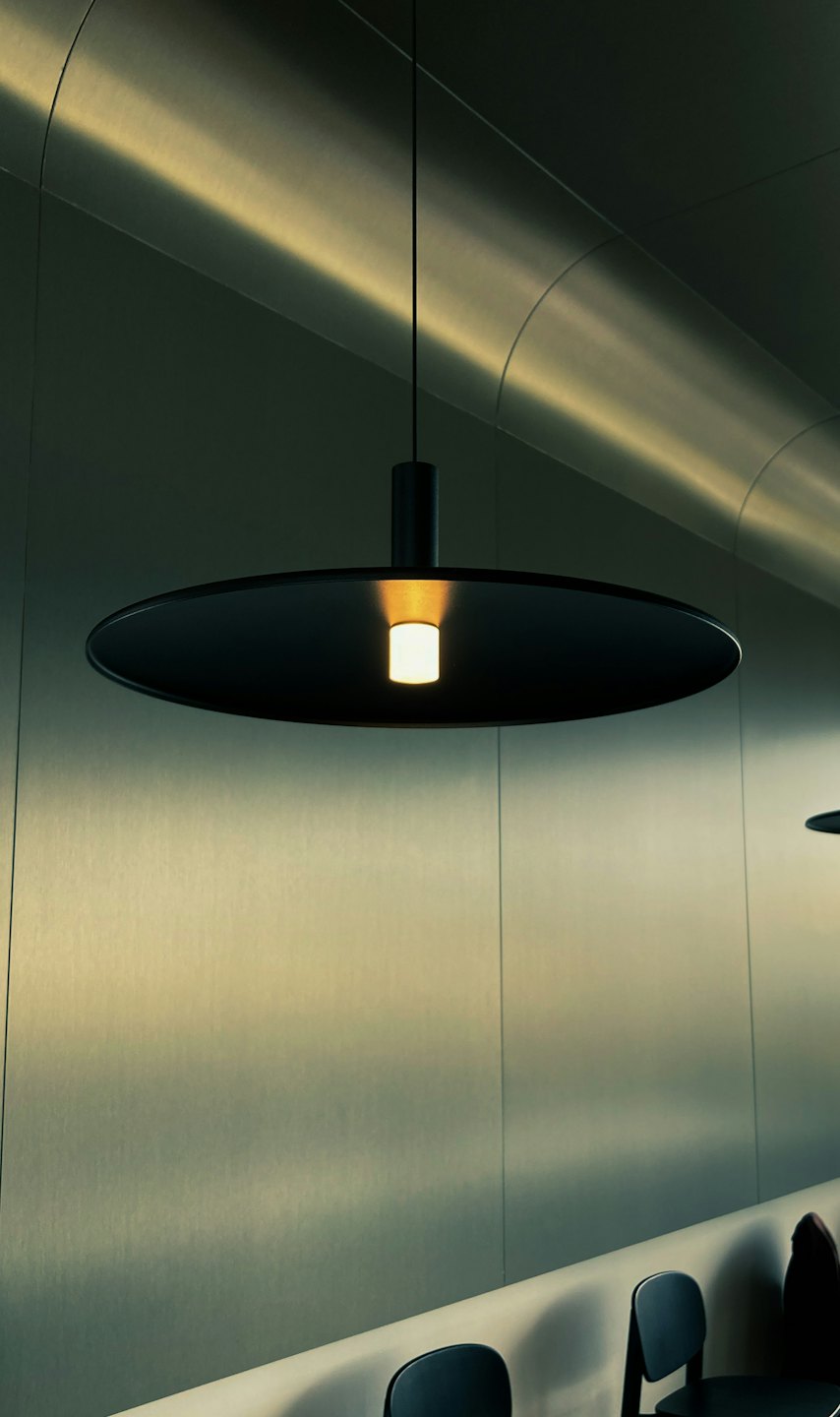 Svart pendellampe lyser opp et moderne rom med metallvegger.